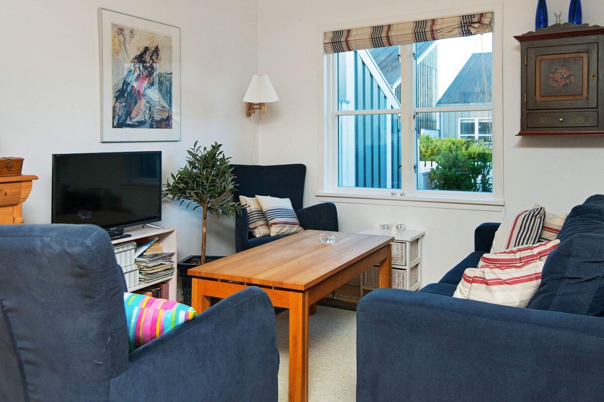 Een woonkamer met een televisie, een bank, een houten tafel en een raam met uitzicht op gebouwen.