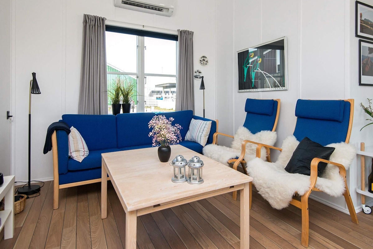 A modern living room with a blue sofa, two blue armchairs, a wooden coffee table, and a small table with two lanterns.