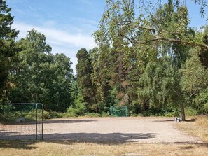 A fenced sports field with a soccer goal, surrounded by dense trees and a clear sky. - 6 Person Holiday Home in Vaeggerlose (Vaeggerlose)