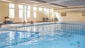 Una piscina interior con techo azulejado, ventanas amplias y algunas sillas de descanso.