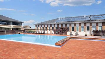 En swimmingpool med liggestole og en bygning med solpaneler.