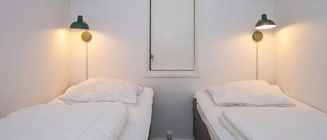 Une petite pièce propre, avec deux lits simples, une porte et deux lampes fixées au mur.