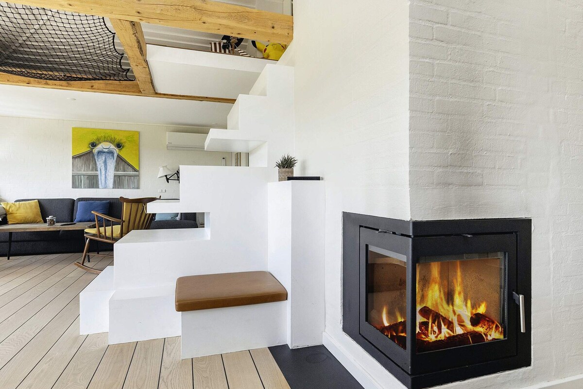 A modern living room with a fireplace, wooden flooring, and a staircase with white walls.