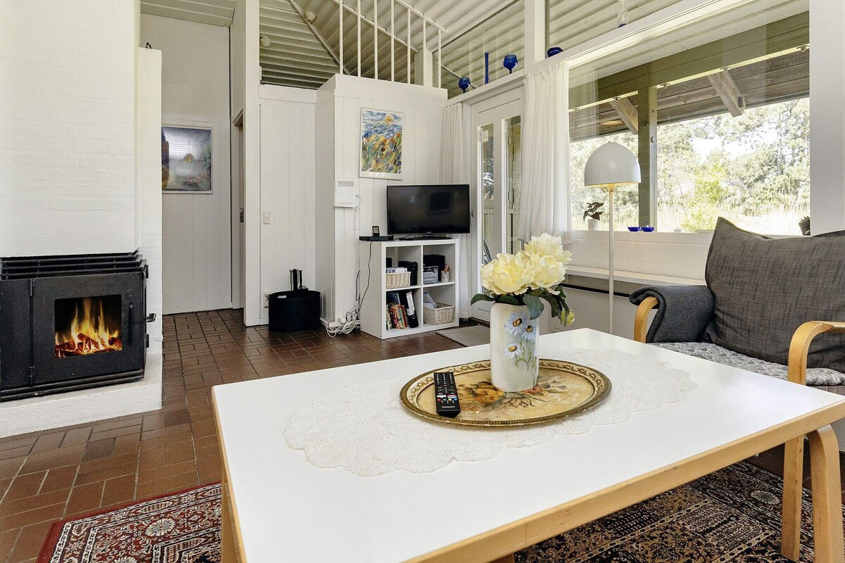 Ett modernt vardagsrum med en öppen spis, ett matbord med en vas med blommor, en soffa och en tv.