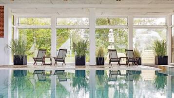 Ein überdachter Swimmingpool mit klaren Glaswänden, umgeben von Topfpflanzen und Korbstühlen.