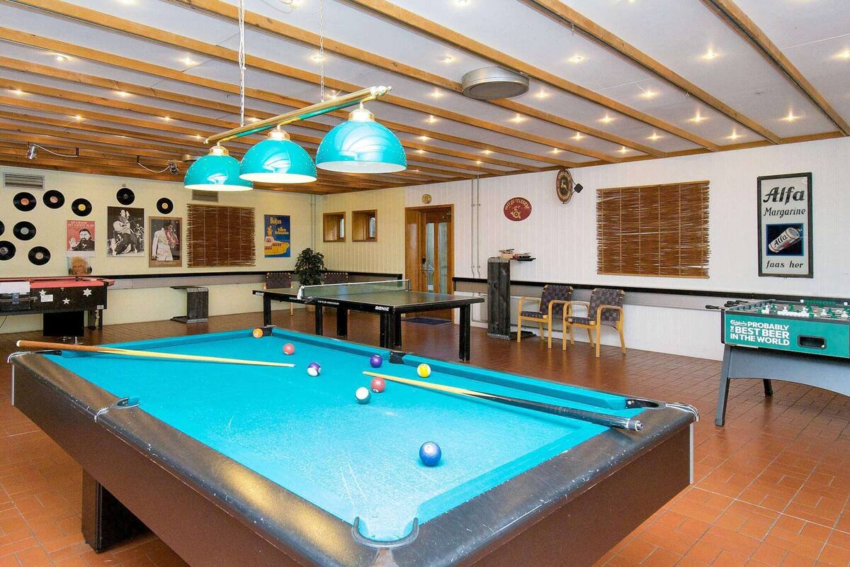 A pool table with balls, a foosball table, and a billiards table in a room with wooden beams and ceiling lights.