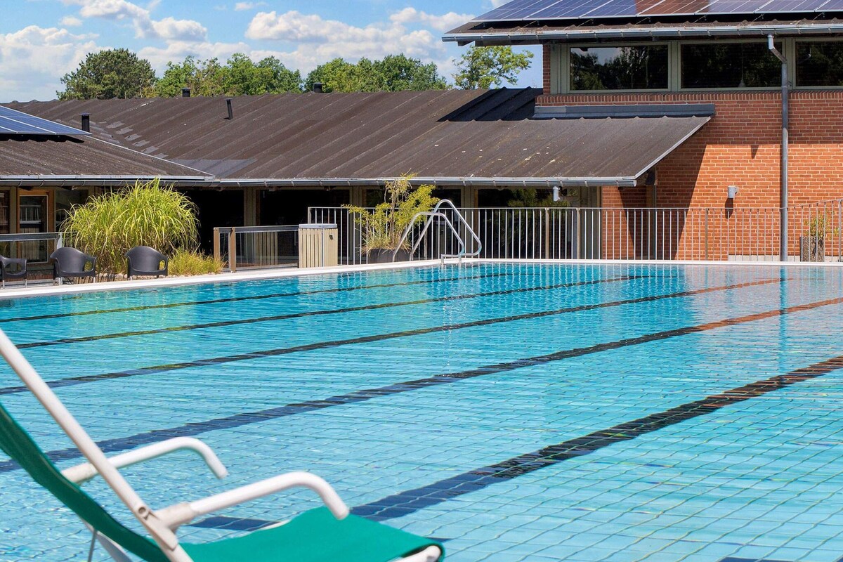 A swimming pool with clear lanes, a green pool chair, and a building with solar panels in the background.