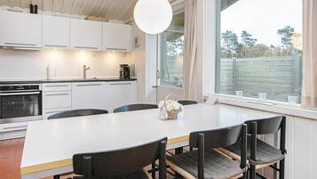 A modern kitchen with white cabinets, a large island with chairs, and a view through a window.