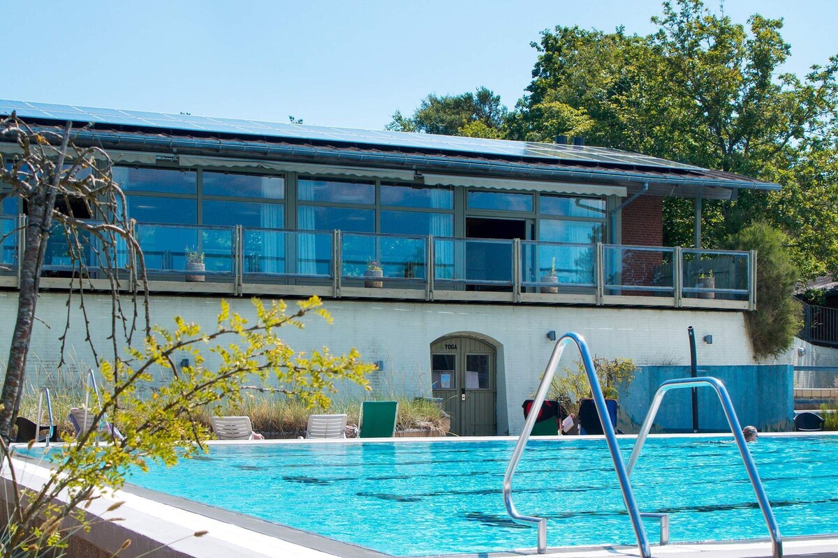 Piscina com escada de metal, porta de yoga e edifício com janelas amplas e varanda.