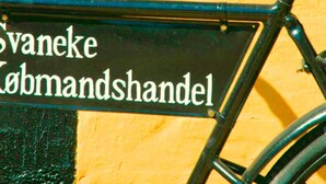 En svart skylt med vit text på en gul vägg.