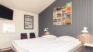 Un lit bien fait, avec du linge de lit blanc, dans une pièce dont un mur est gris et qui est décorée d’un collage d’affiches.
