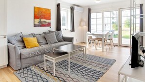 A modern living room with a grey sofa, a coffee table, a TV, and a dining area with chairs and a table. - 4 Star Holiday Home in Laeso (Læsø)