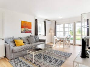 A modern living room with a grey sofa, a coffee table, a TV, and a dining area with chairs and a table. - 4 Star Holiday Home in Laeso (Læsø)