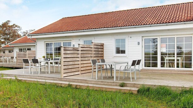 A white building with a red-tiled roof, large windows, and outdoor seating with chairs and tables. - 4 Star Holiday Home in Laeso (Læsø)