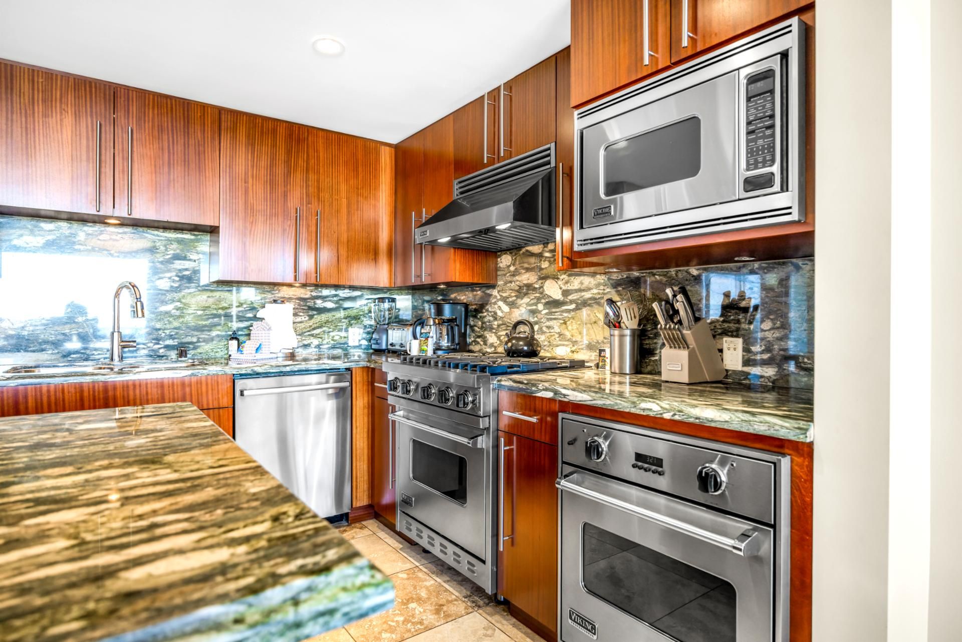 Una cocina moderna con gabinetes de madera, encimera de granito, microondas integrado, estufa y lavavajillas.