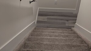 Una escalera con alfombra y acabado de madera en la parte inferior, paredes blancas y una barandilla a la izquierda.