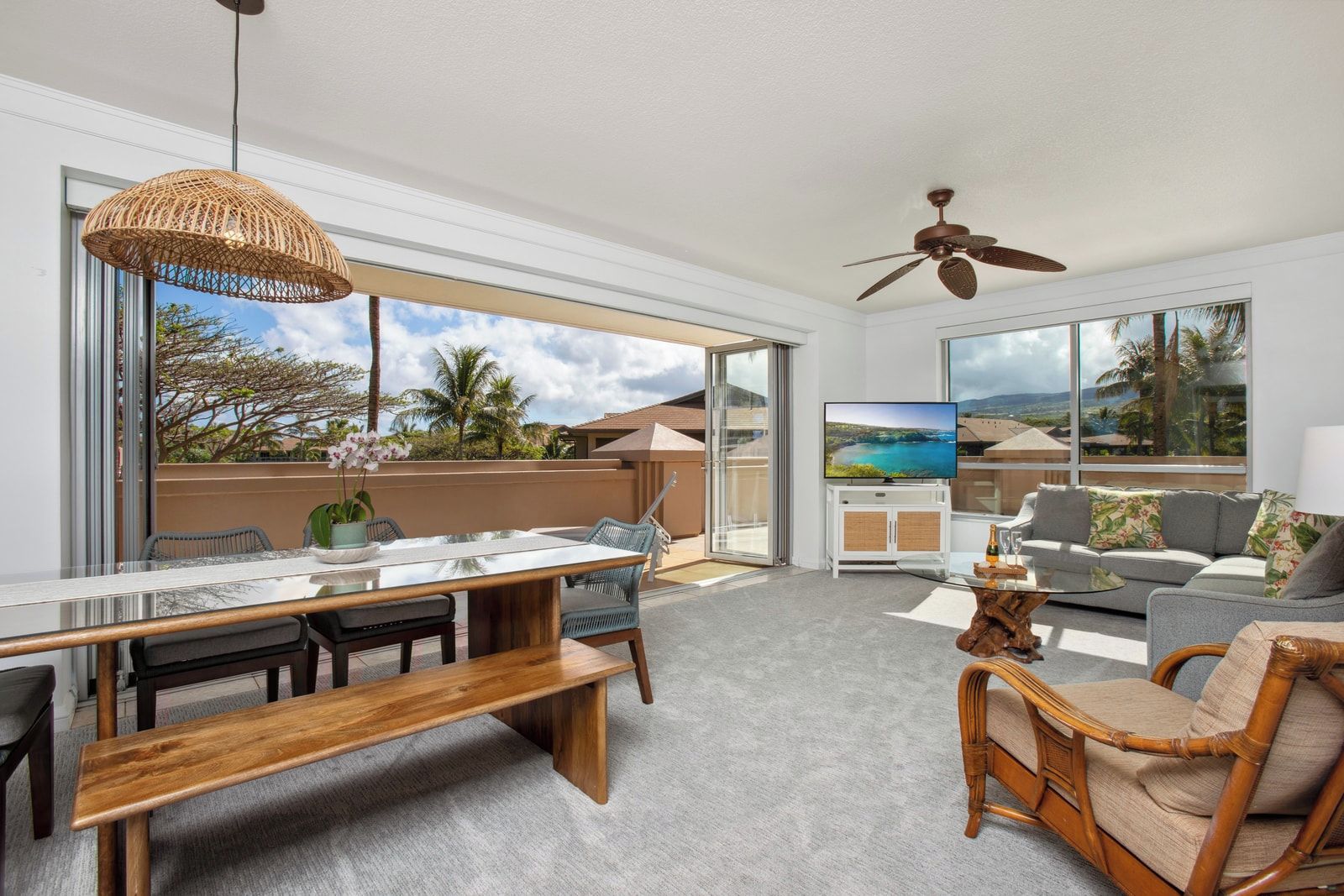 A spacious living area with a dining table, seating, a television, and a balcony with a view.