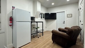 A compact living space with a kitchenette, a flat-screen TV, a leather recliner, and a fire extinguisher. - Charming 1-bedroom house in perfect Fort Morgan Walking distance to downtown (Fort Morgan)