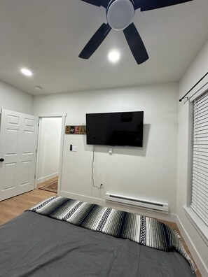 A bedroom with a bed, a ceiling fan, a mounted TV, and a door. - Charming 1-bedroom house in perfect Fort Morgan Walking distance to downtown (Fort Morgan)