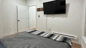 A bedroom with a bed, a ceiling fan, a mounted TV, and a door. - Charming 1-bedroom house in perfect Fort Morgan Walking distance to downtown (Fort Morgan)