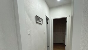 A hallway with white walls, a wooden floor, and a patterned rug. There is a door at the end of the hallway. - Charming 1-bedroom house in perfect Fort Morgan Walking distance to downtown (Fort Morgan)