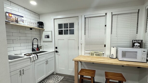 A compact kitchen with white cabinets, a wooden countertop, a microwave, and a sign that reads "Please seat yourself." - Charming 1-bedroom house in perfect Fort Morgan Walking distance to downtown (Fort Morgan)
