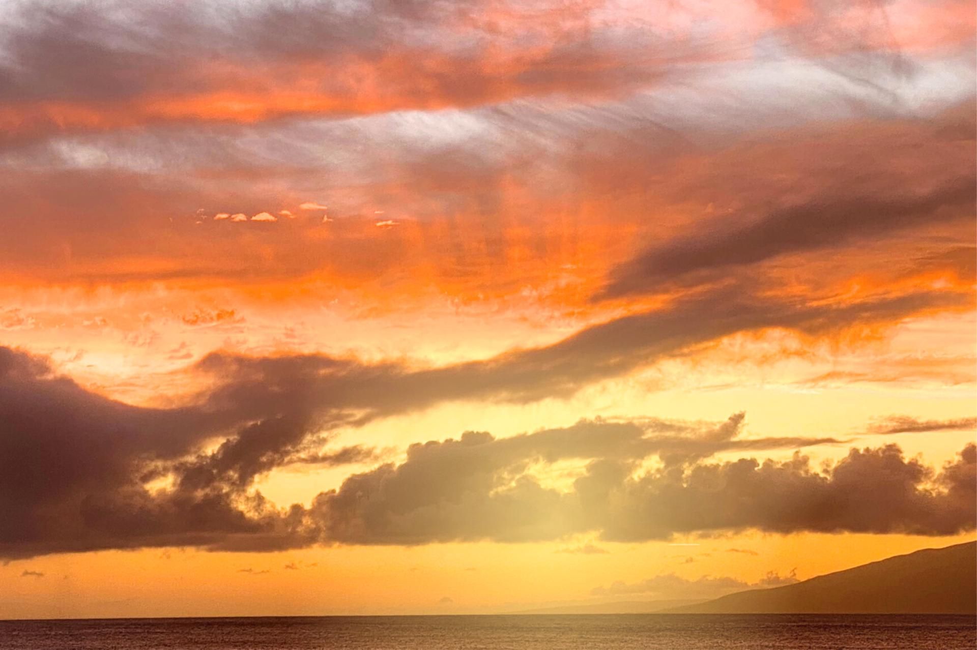 Un coucher de soleil sur une étendue d’eau, avec des nuages dans le ciel.