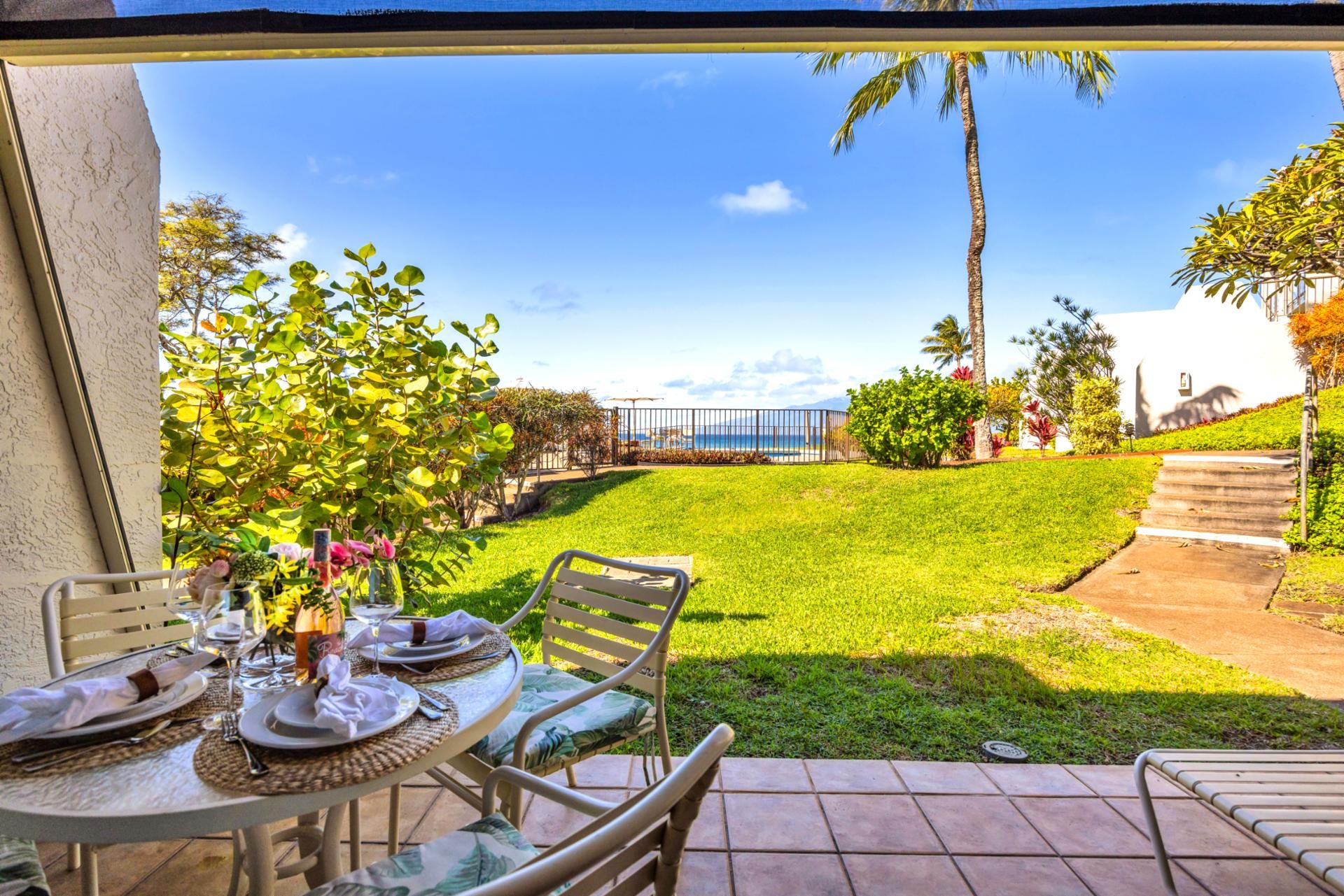 Une terrasse avec une table dressée pour le repas, donnant sur une pelouse bien entretenue et offrant une vue sur l’océan.
