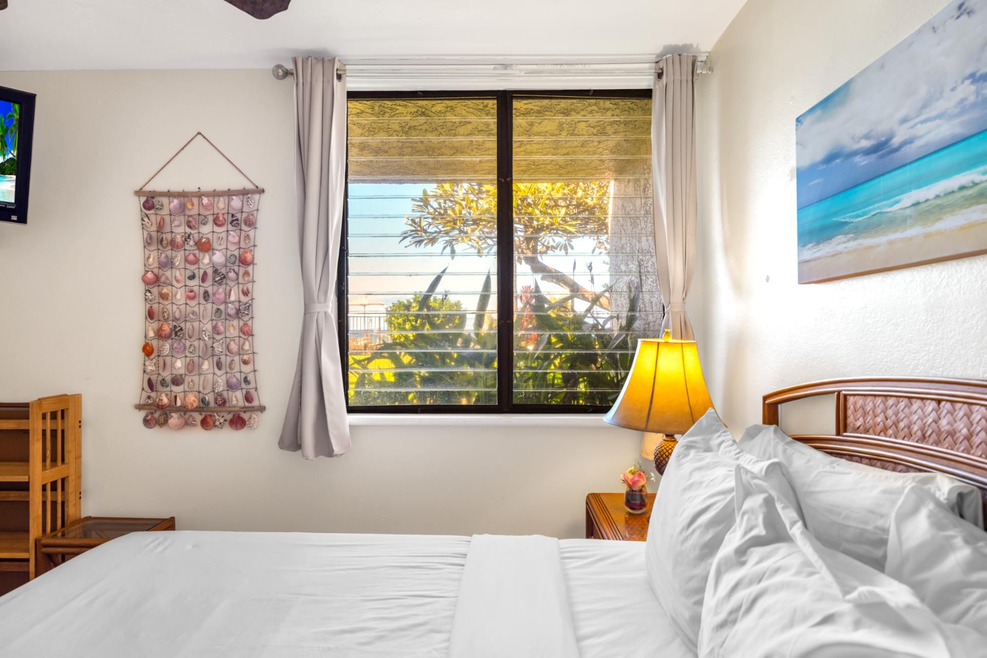 A bedroom with a bed, a window with curtains, a wall hanging, a lamp, and a painting.
