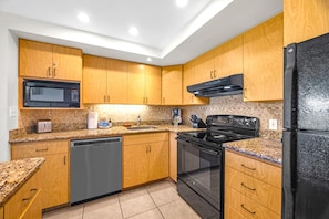 A modern kitchen with wooden cabinets, a black refrigerator, a microwave, a coffee maker, and a dishwasher. - Napili Point | Ocean View 1 BR | Water Front | Car Incl. w/ 6+ Nights | NAP-A24 by KBM (Lahaina)
