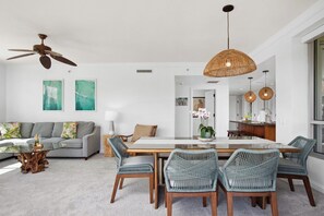 A modern living room with a sofa, a dining table with chairs, a ceiling fan, and a kitchen area visible through an open doorway. - Honua Kai | Ocean View 3 BR, Sleeps 10 | Car Incl. w/ 6+ Nights | HKH ML-1922 by KBM (Lahaina)