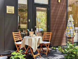 Un espace extérieur aménagé avec deux chaises en bois et une table, une porte vitrée portant un numéro, et un petit parasol.
