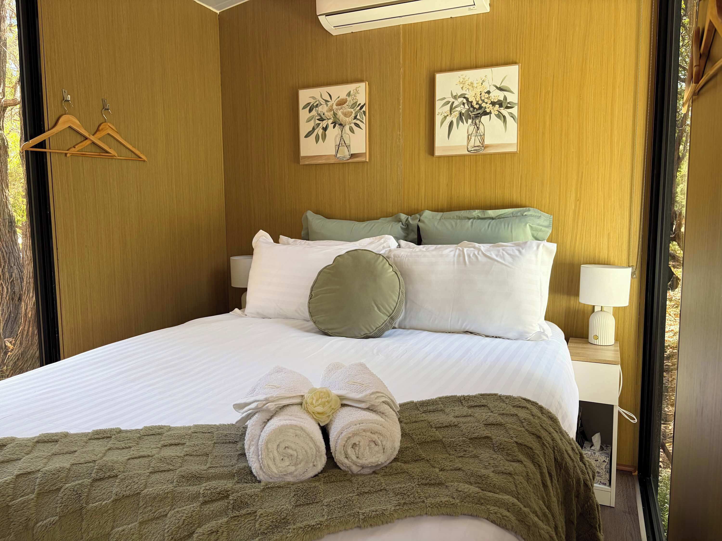 A neatly made bed with pillows, a towel, and a bedside table with a lamp.