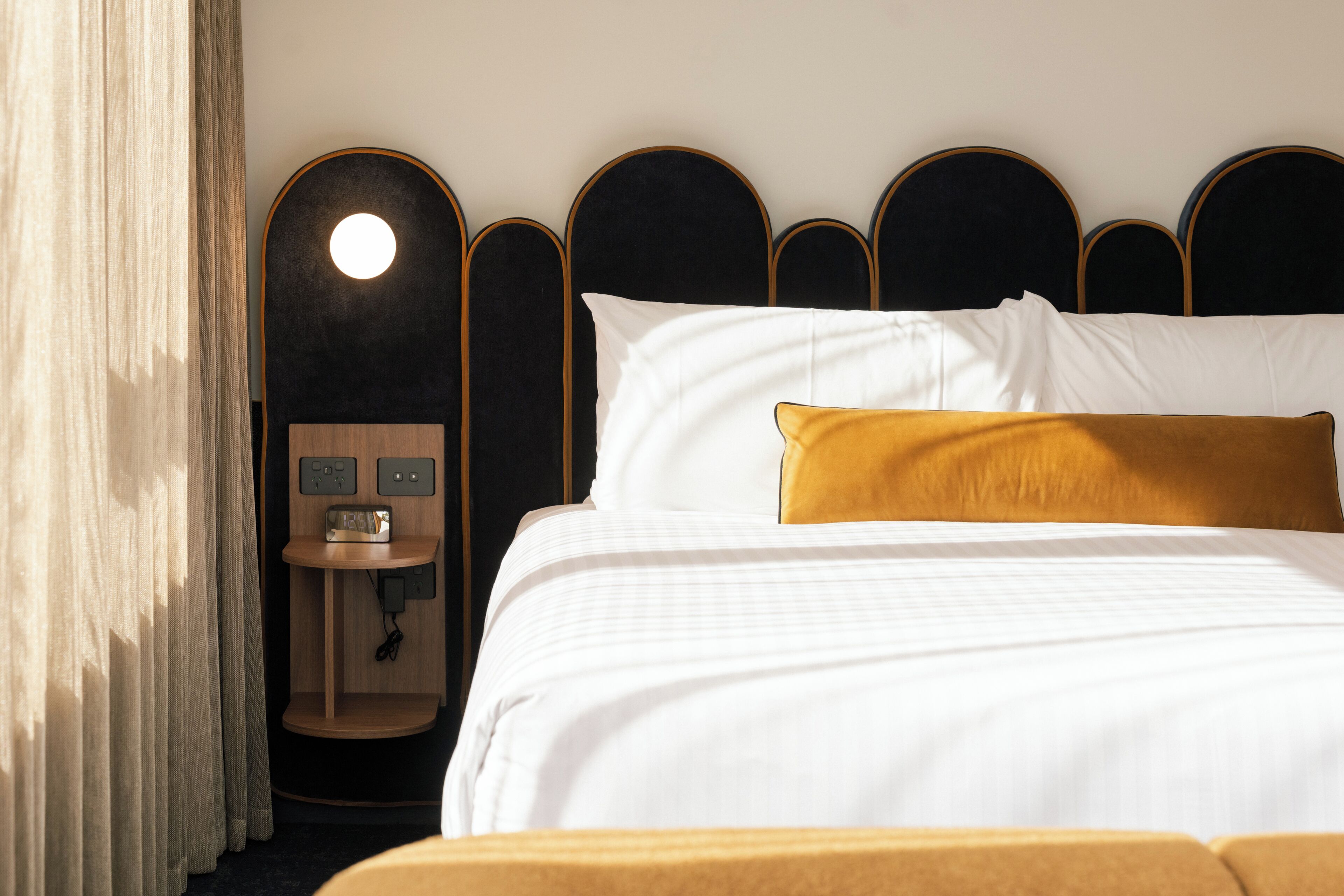 A hotel room with a bed, a bedside table with a radio, and a wall-mounted light.