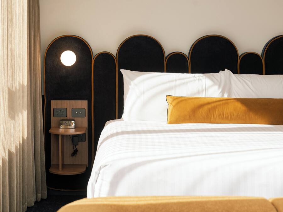 A hotel room with a bed, a bedside table with a radio, and a wall-mounted light.