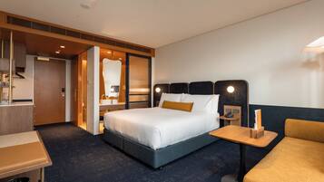 Une chambre d’hôtel comprenant un lit, une table de chevet, une chaise, un bureau et une salle de bain avec douche et lavabo.