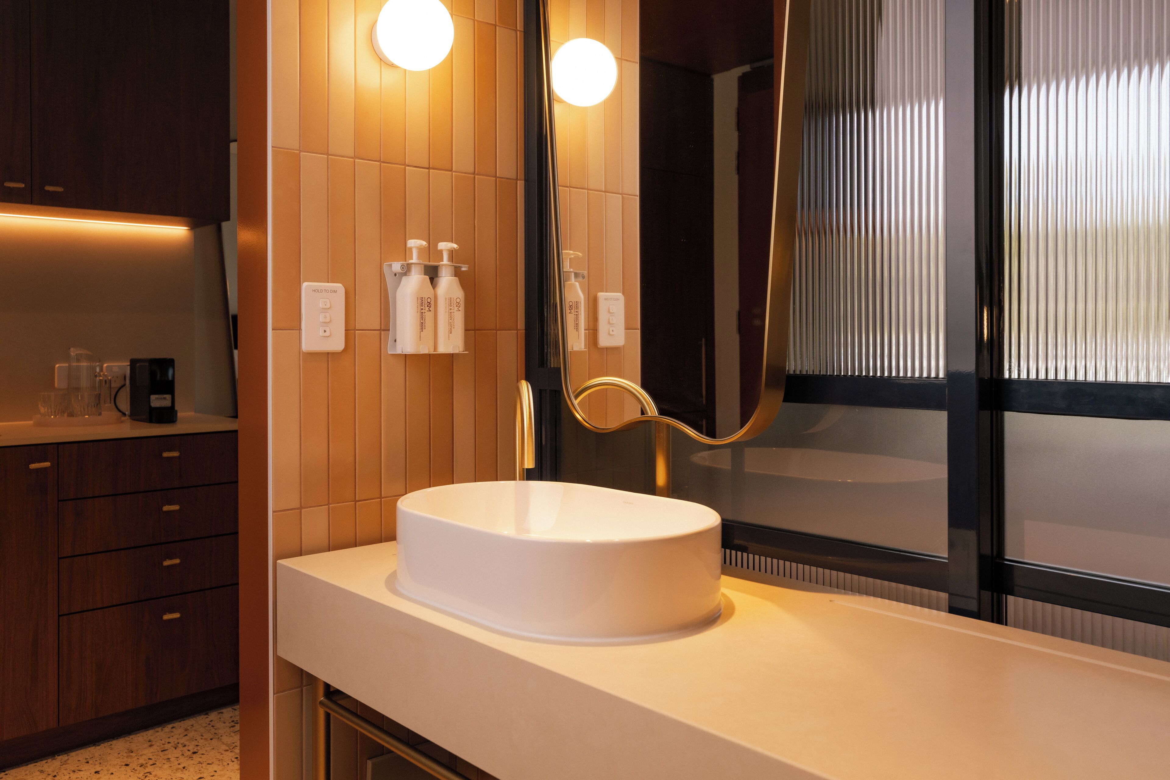 A modern bathroom with a round white sink, wooden cabinetry, and a large mirror.