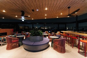 A modern bar area with seating, a central planter, and a city view.