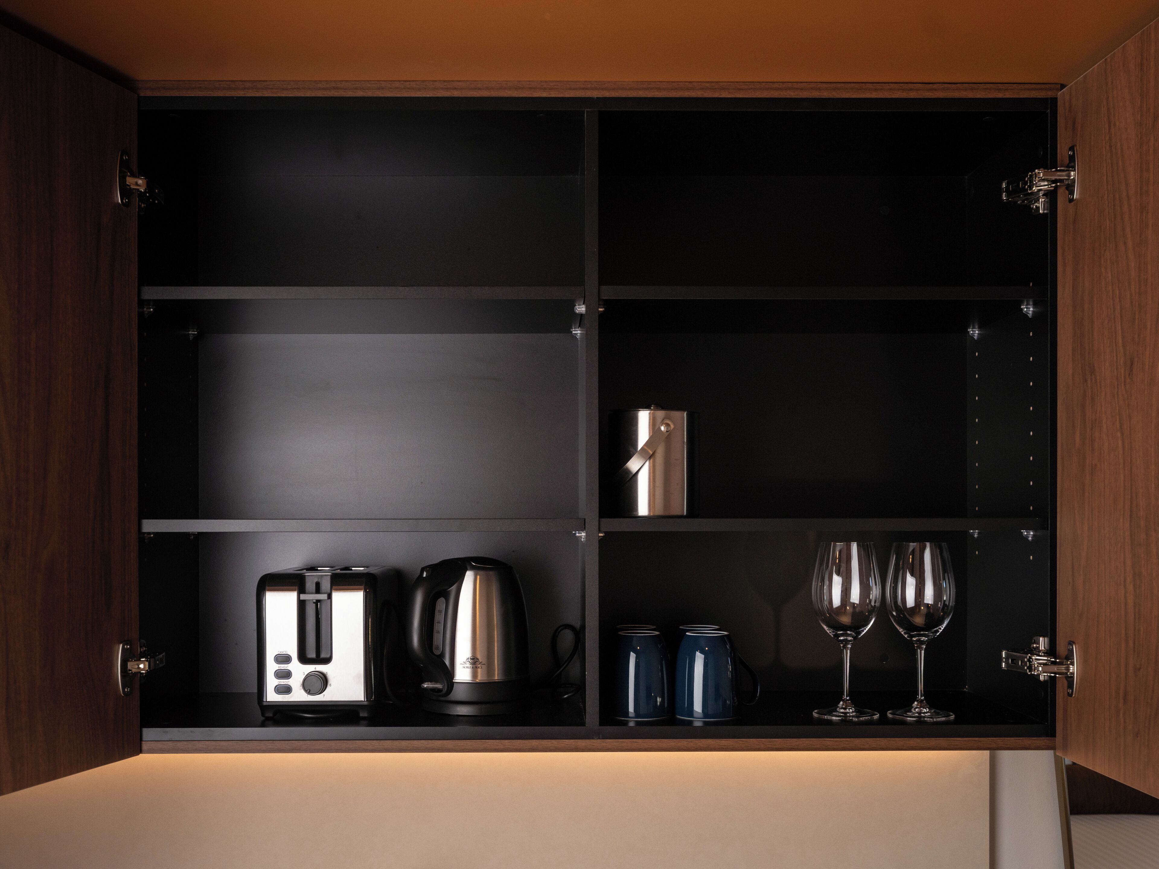 Un meuble de cuisine contenant un grille-pain, une bouilloire, deux tasses et deux verres à vin.