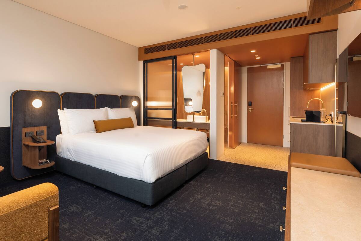 A hotel room with a bed, bedside table, lamp, chair, and a view of the bathroom.