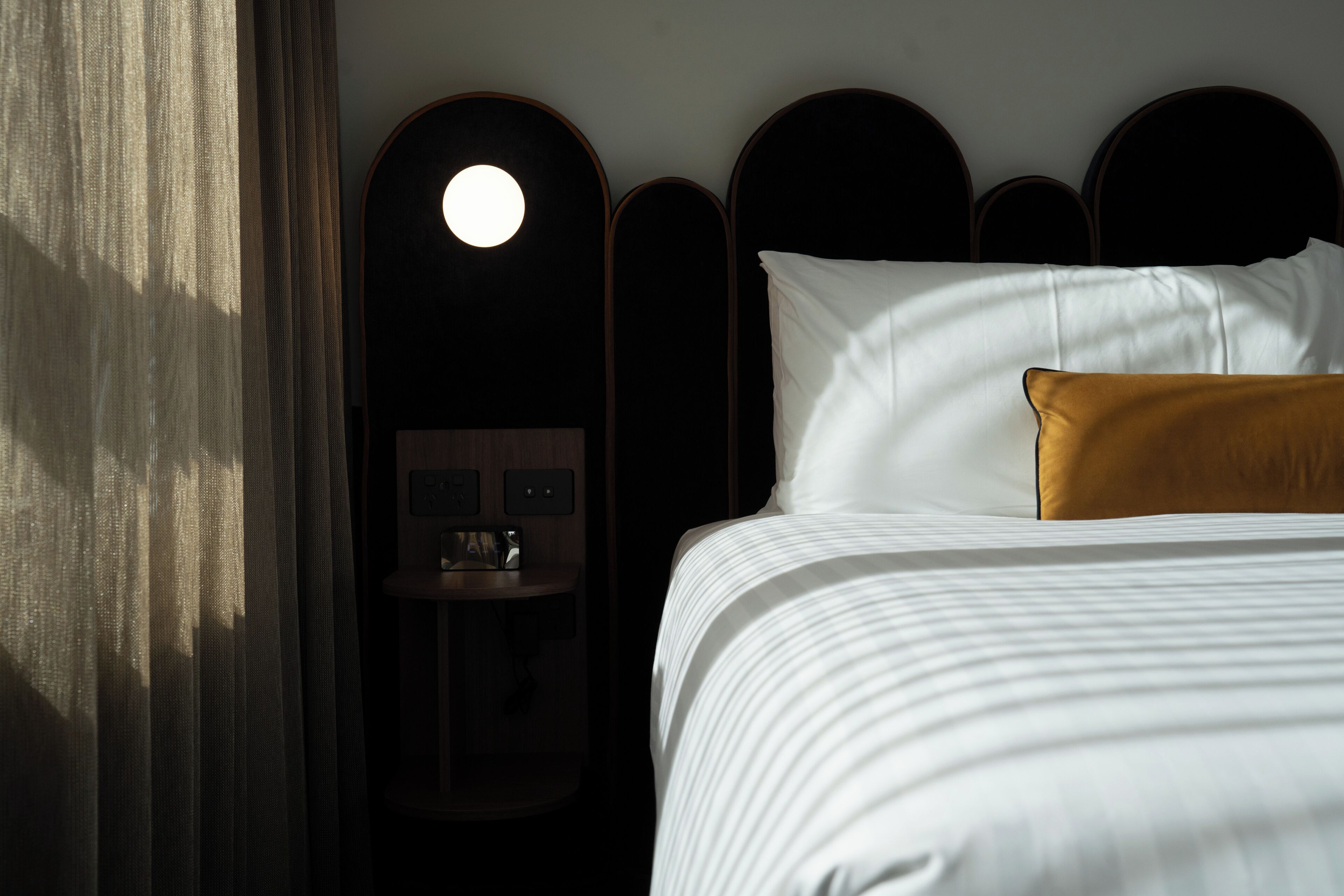 A hotel room with a bed, a nightstand, and a wall-mounted light fixture.