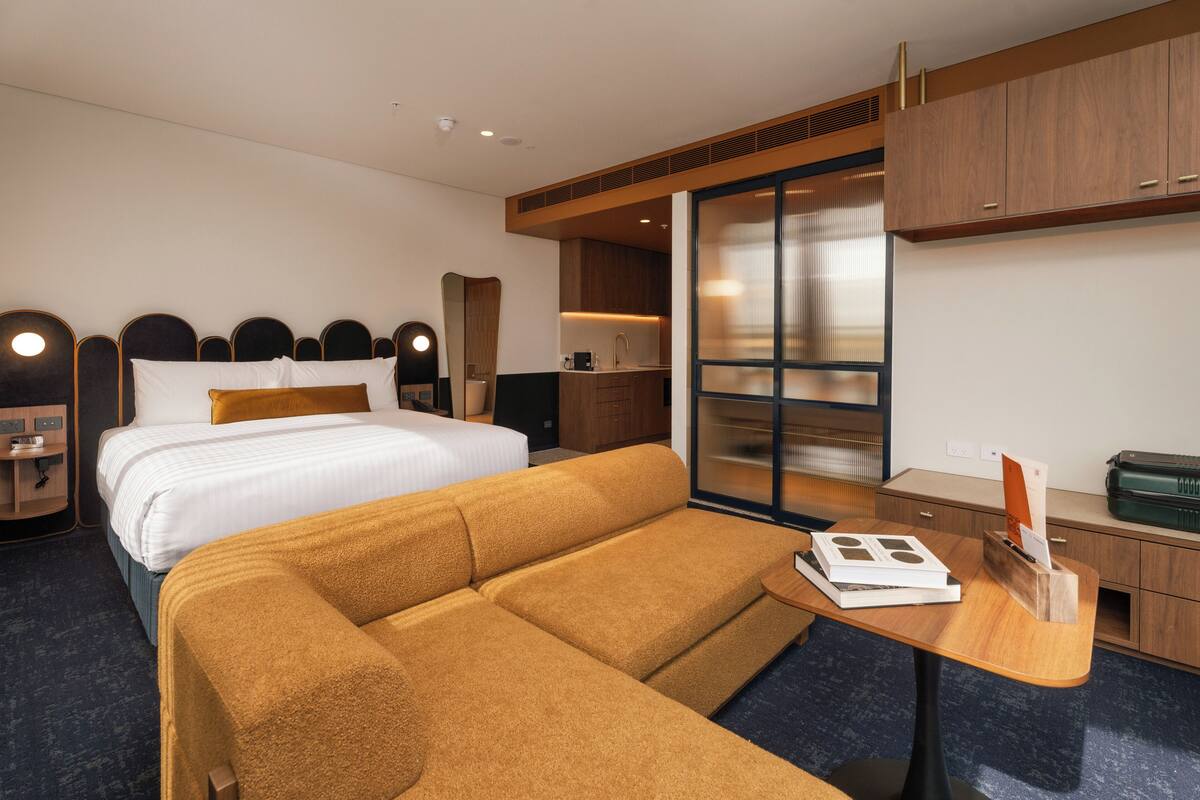 A hotel room with a bed, a sofa, a desk, a mirror, a wardrobe, and a sliding door.