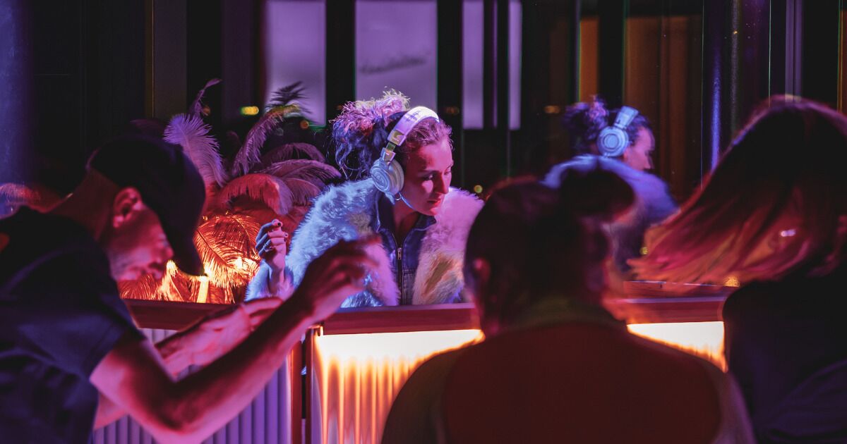 A group of people dancing in a dimly lit room with a bar area.