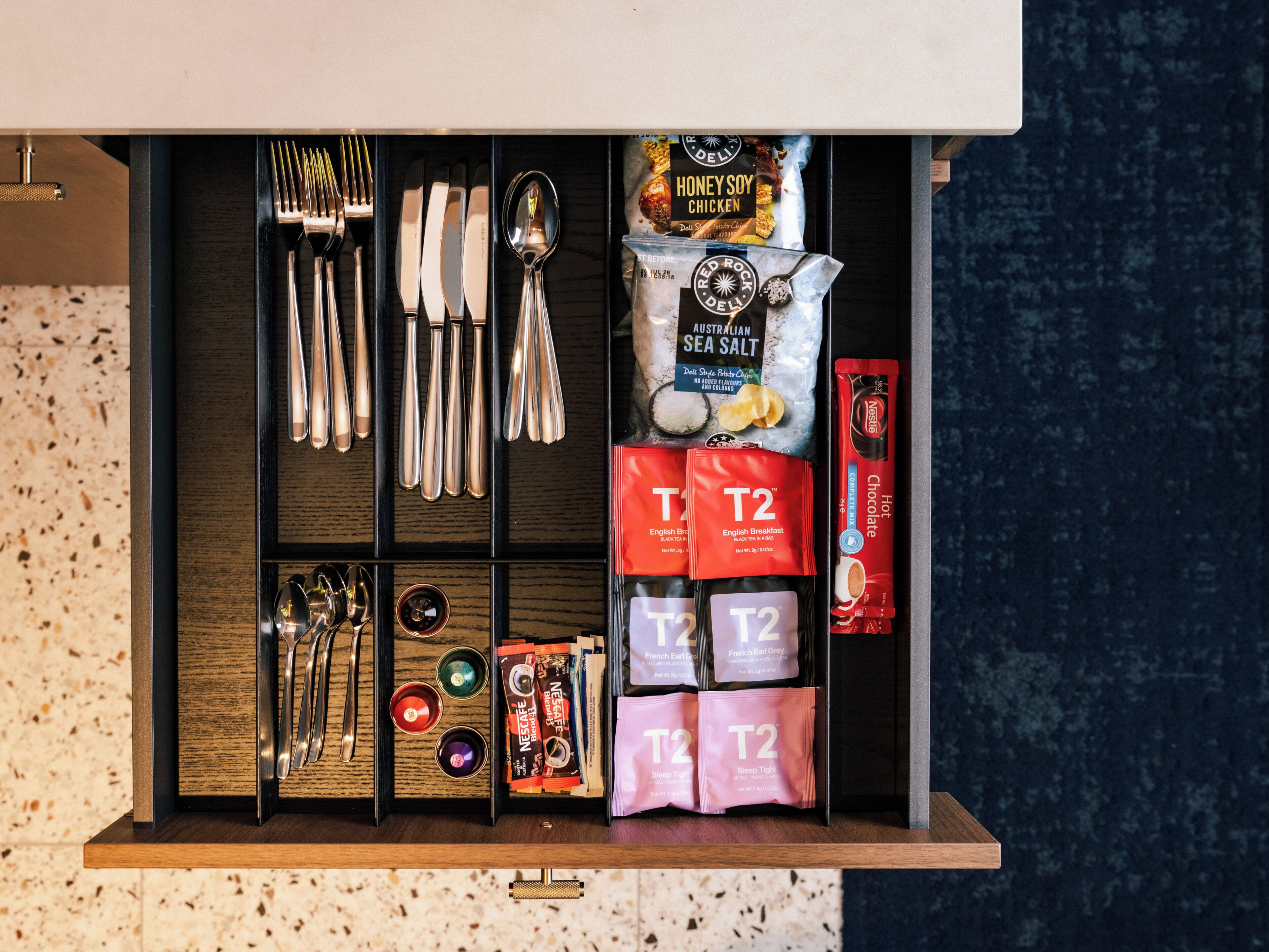 A drawer with neatly organized kitchen utensils, tea bags, and a packet of sea salt.