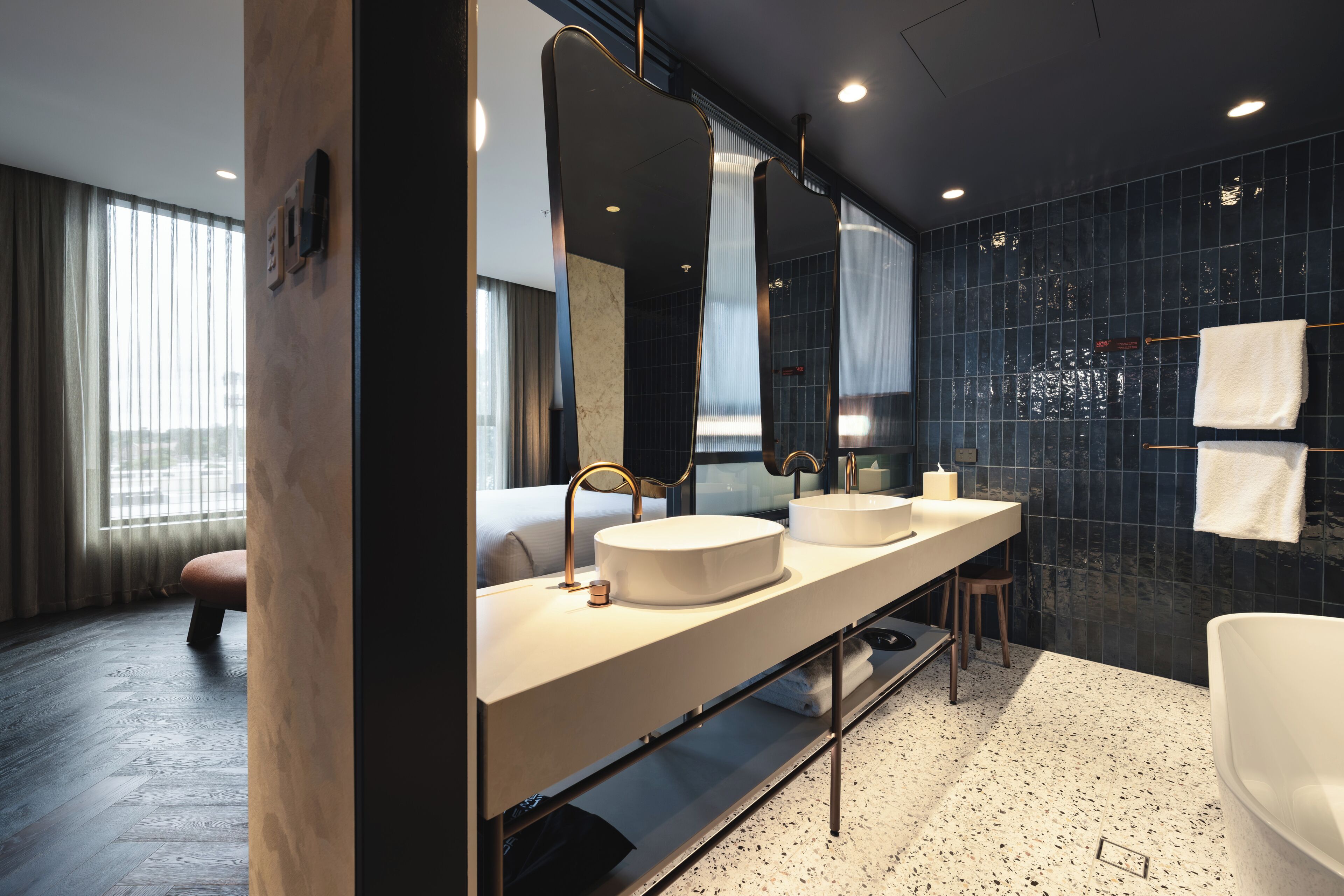 Une salle de bain moderne avec un double lavabo, de grands miroirs, une baignoire et une vue sur la ville par la fenêtre.