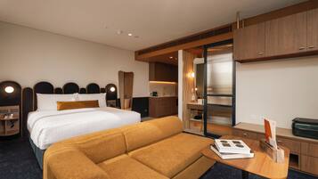 Habitación de hotel con cama, sofá, mesitas de noche, un espejo y una zona de kitchenette.