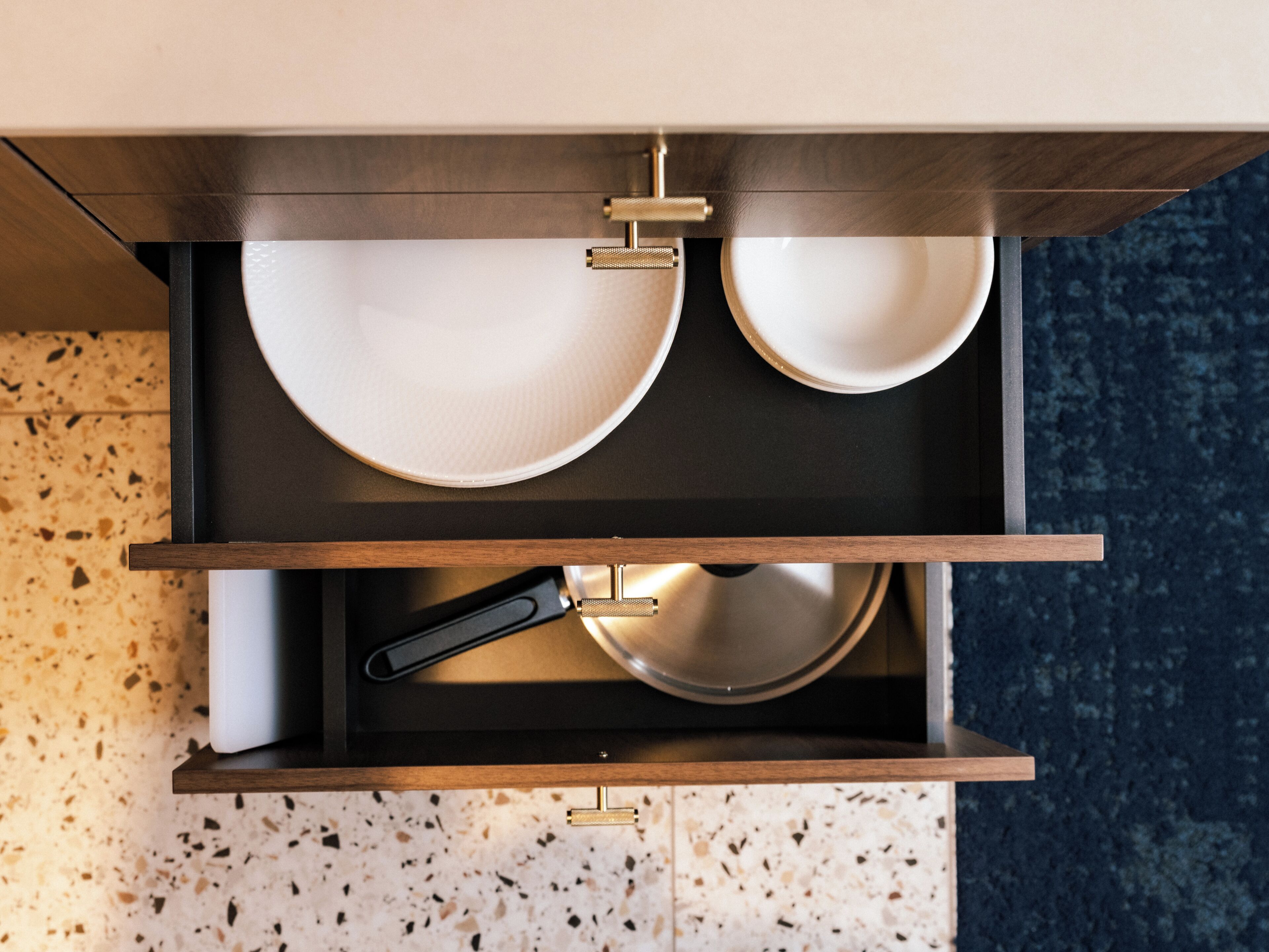 A kitchen drawer with two white plates, a black frying pan, and a metal utensil.