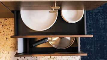 A kitchen drawer with two white plates, a black frying pan, and a metal utensil.