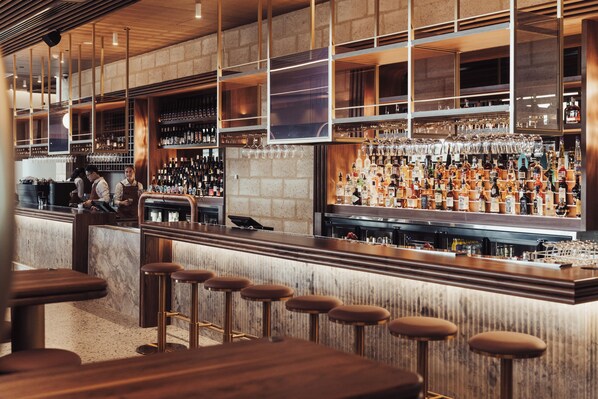A bar area with a counter, stools, and shelves stocked with bottles and glasses.