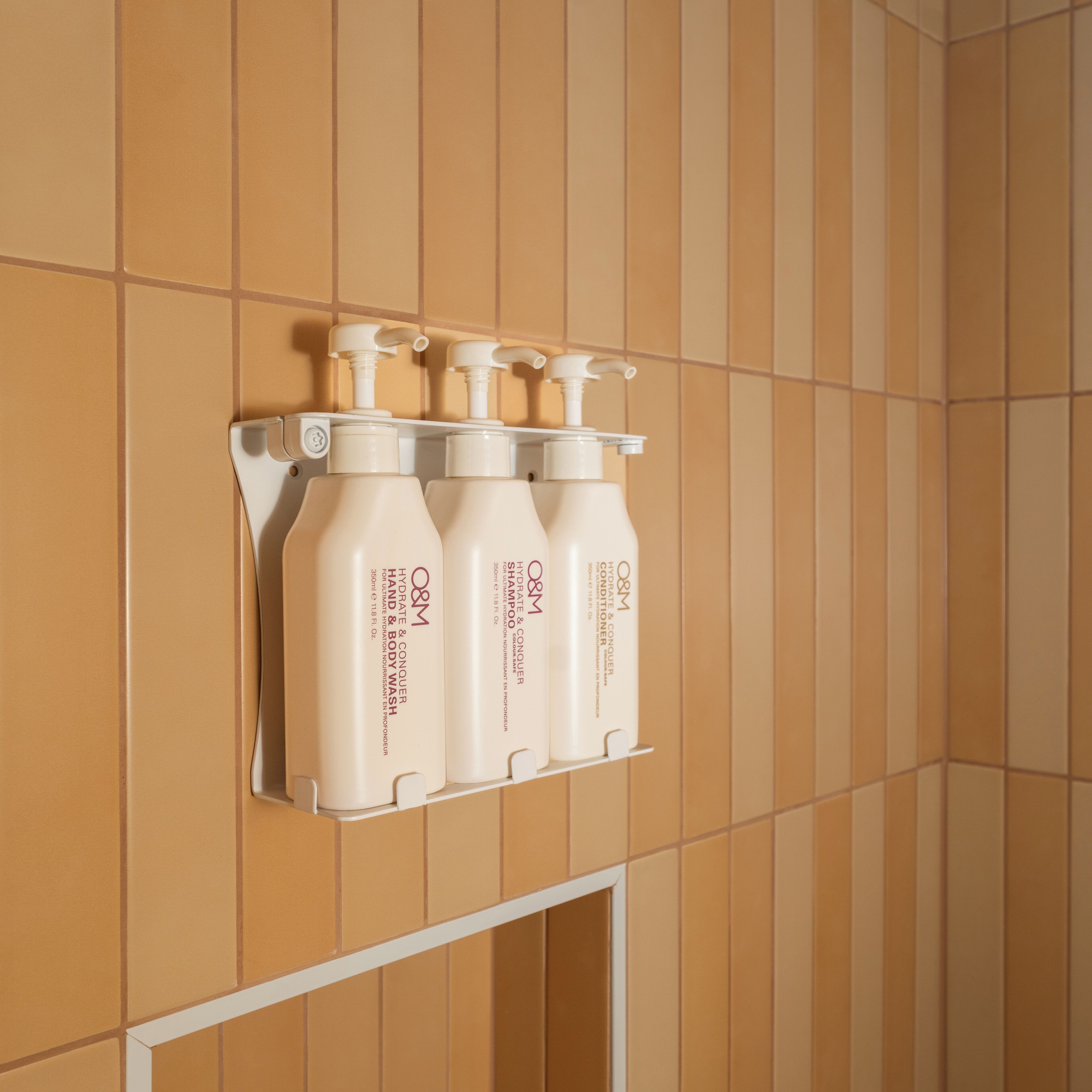 Un baño con dispensador mural que contiene tres botellas de jabón de manos y cuerpo O&M.